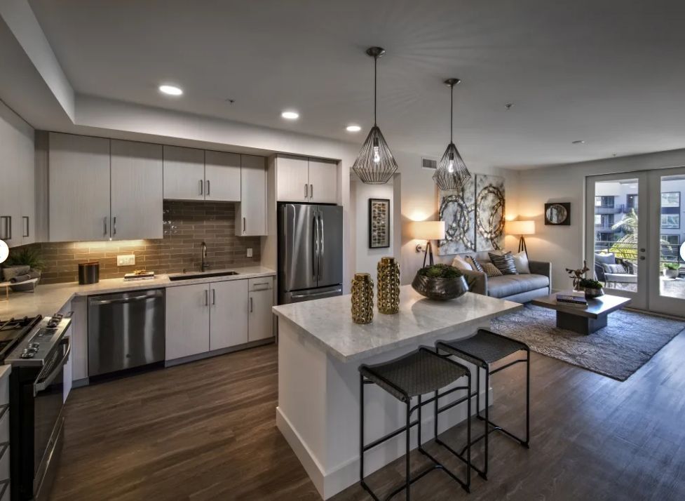 A kitchen with white cabinets , stainless steel appliances , and a large island in the middle of the room.