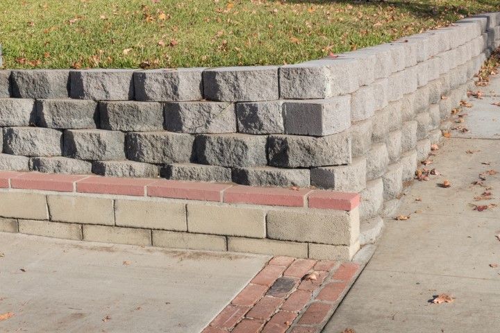Stone retaining wall with a red and tan brick base, beside a concrete sidewalk.