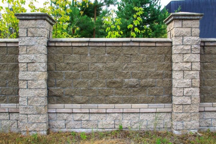 Stone fence with decorative pillars and a backdrop of trees.