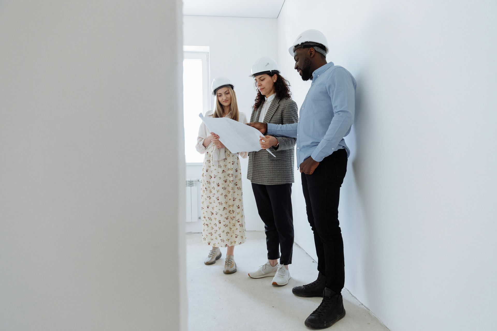 Three people in hard hats reviewing blueprints in a white room.