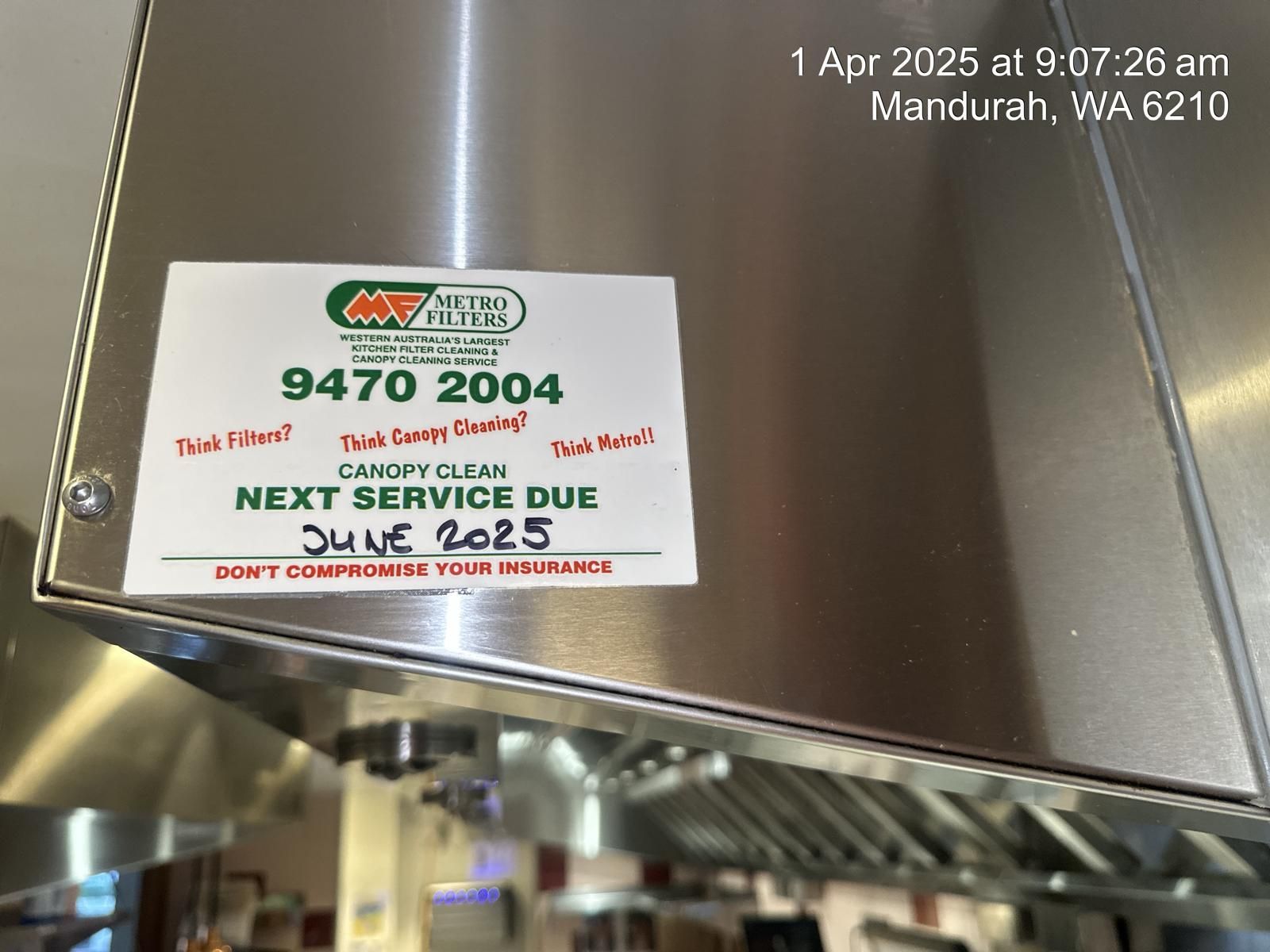 Stainless steel kitchen canopy with a service label.  Next service due June 2025.