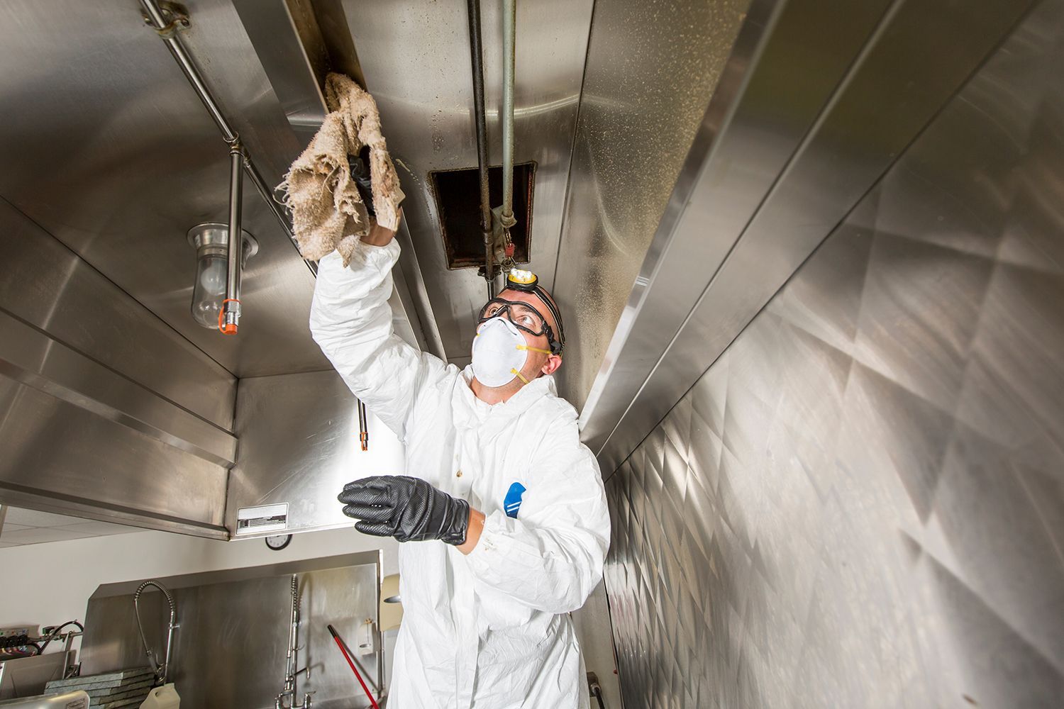 A professional cleaning a commercial kitchen exhaust system.