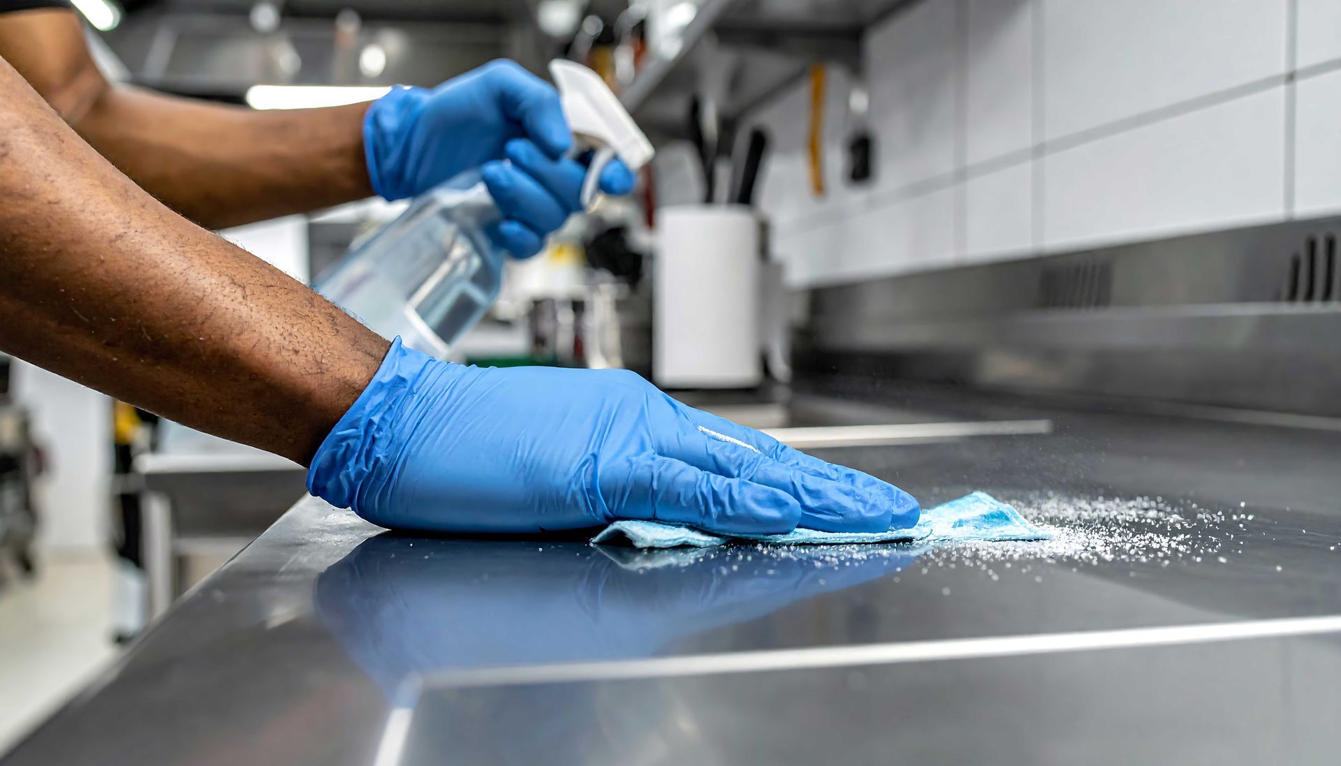 Blue-gloved hands cleaning a stainless steel counter in a commercial kitchen