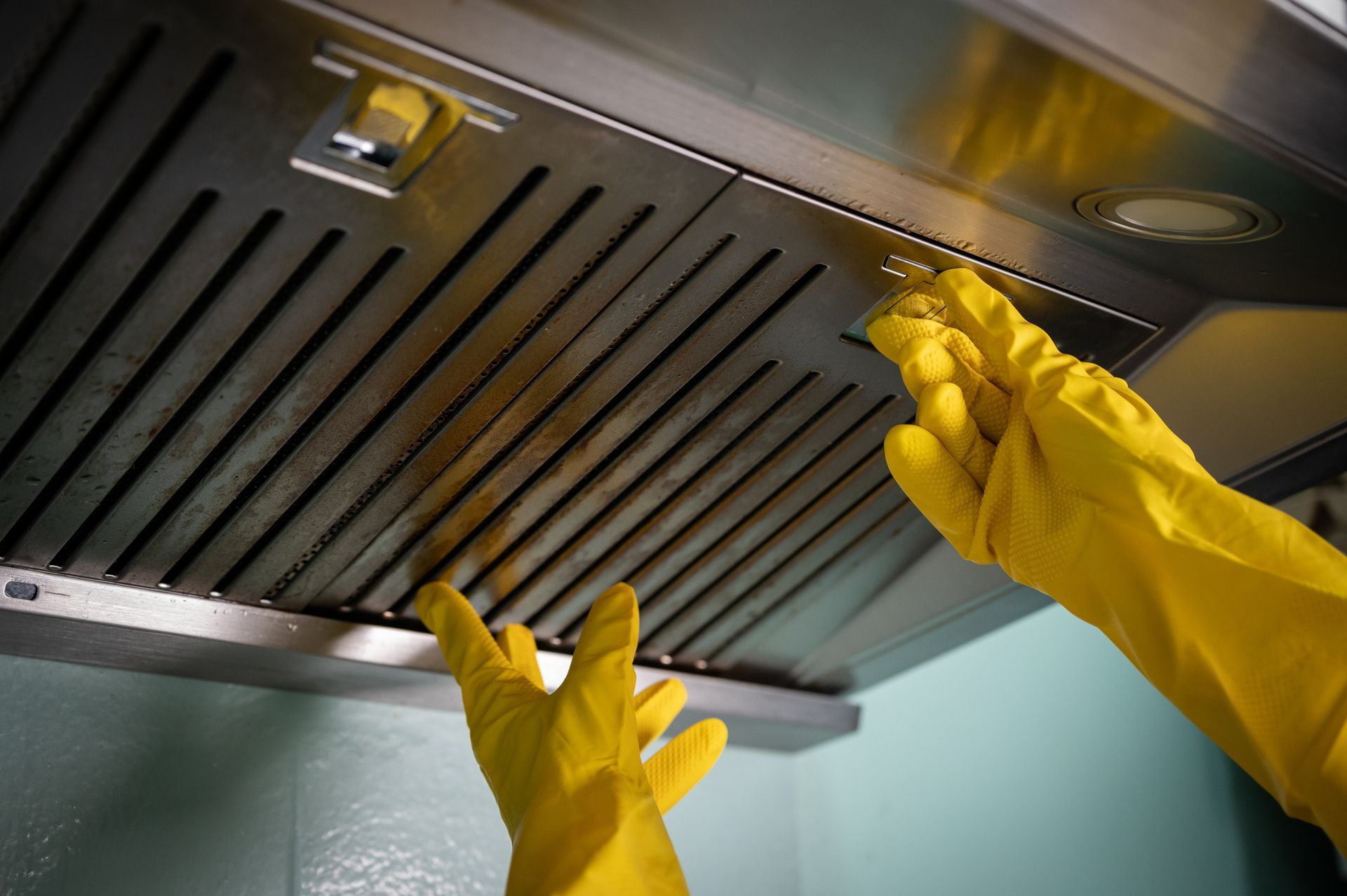 A close-up of a worker with rubber gloves cleaning filters in a commercial kitchen. A close-up of a worker with rubber gloves cleaning filters in a commercial kitchen.