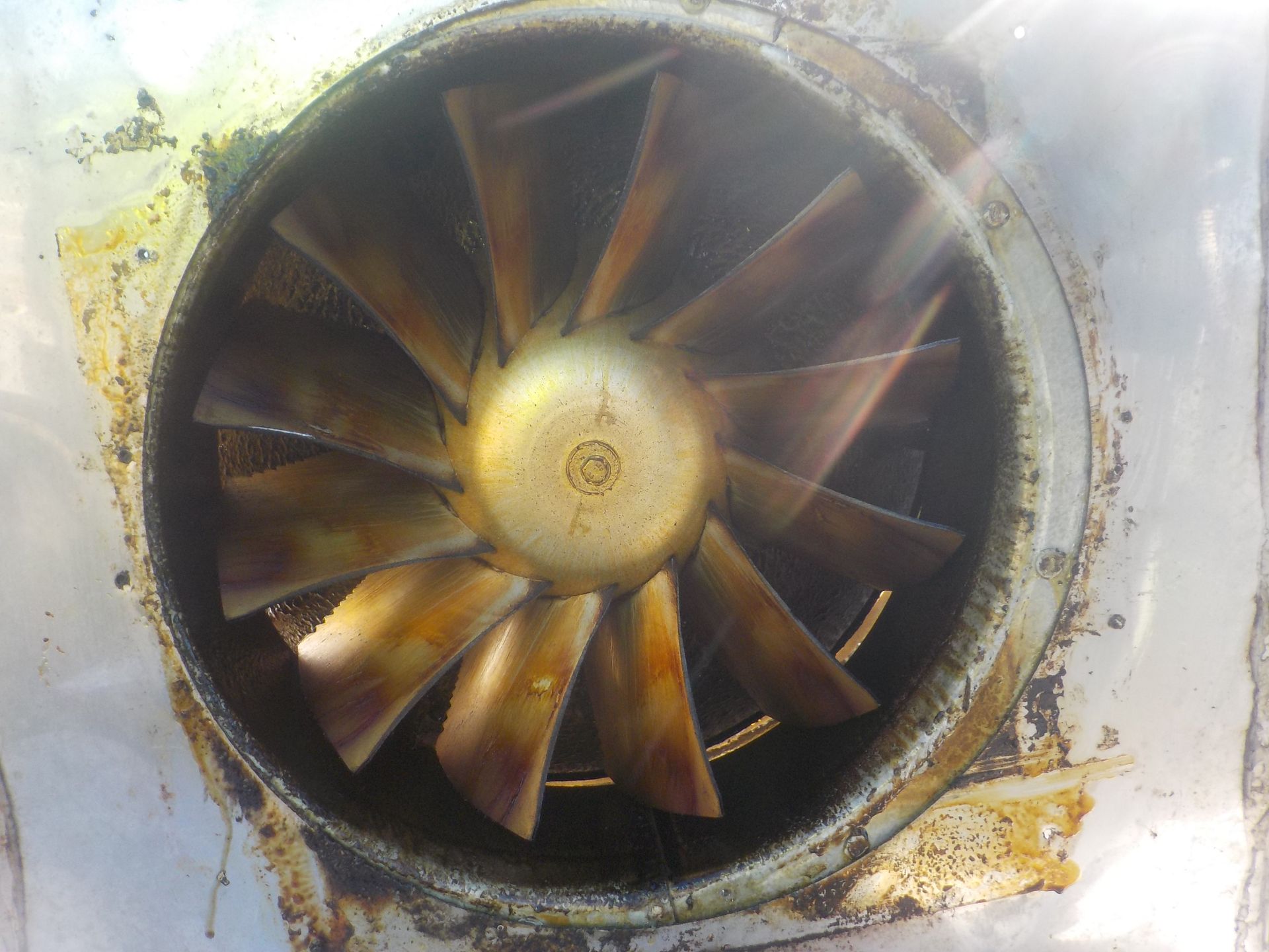 Fan blade assembly with brown-stained blades inside a metal casing, viewed directly.
