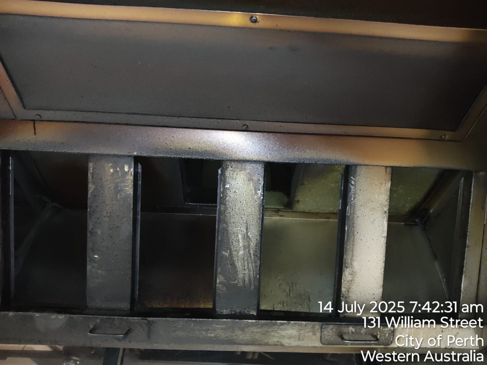 Inside of a commercial kitchen exhaust hood; dirty metal filters.