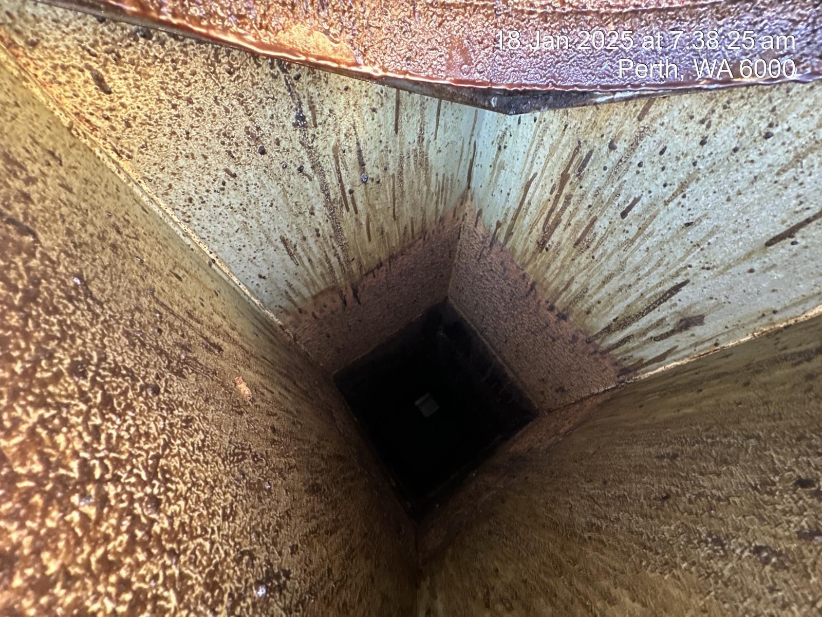 Looking down a narrow, dark shaft with rusty, stained walls.