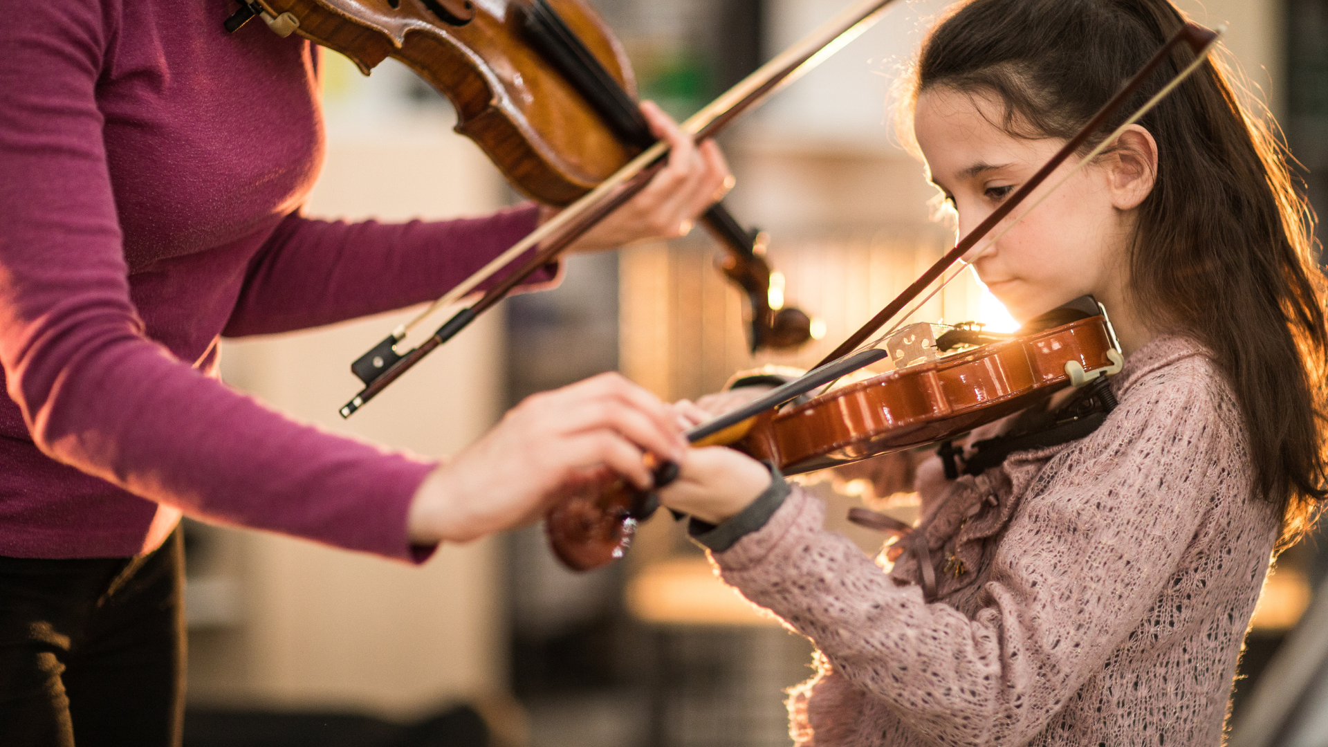A woman is teaching a young girl how to play the violin.