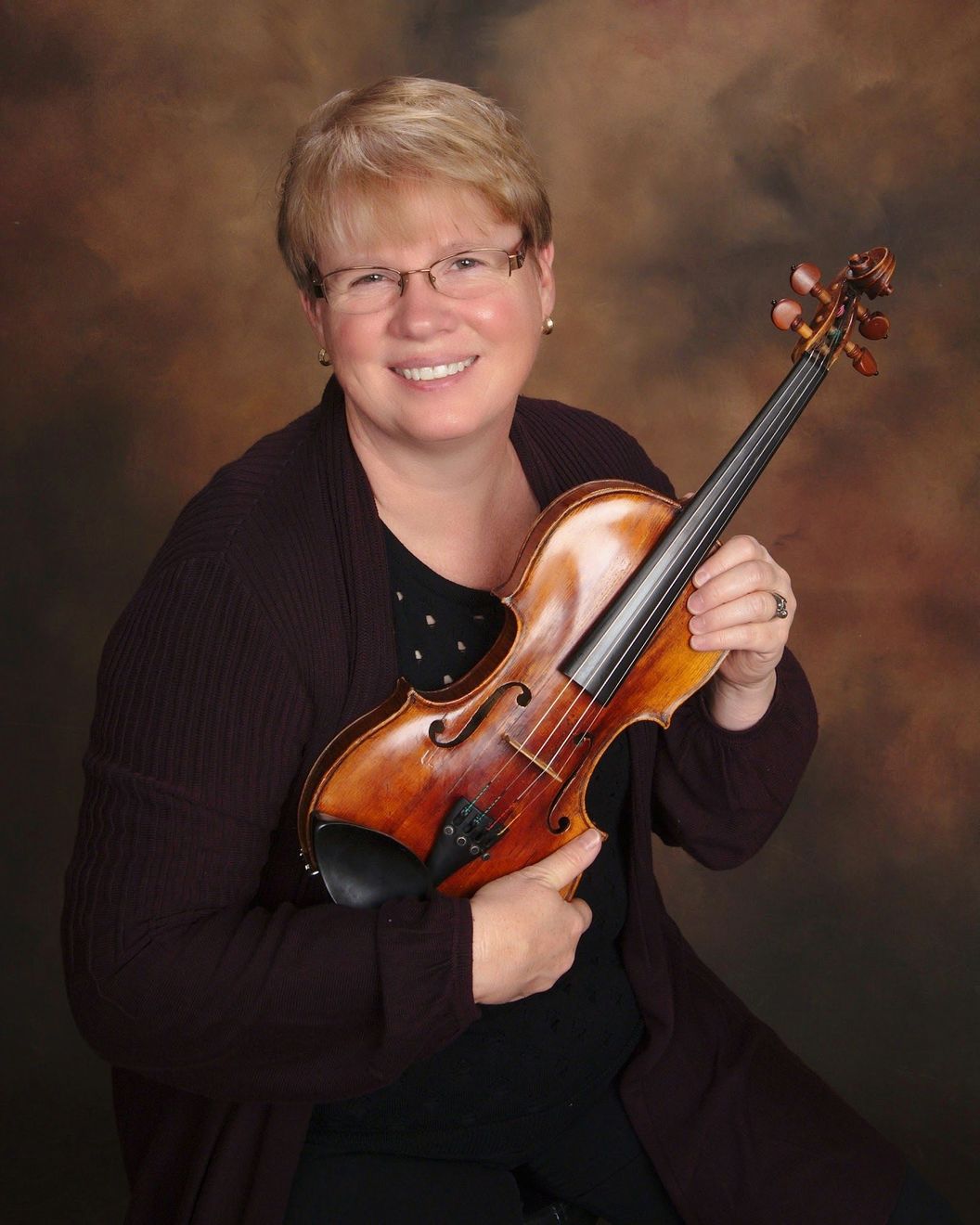 A woman is holding a violin and smiling for the camera