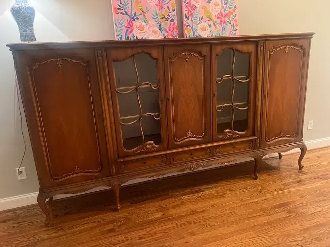 A wooden cabinet with glass doors is sitting on a wooden floor in a living room.