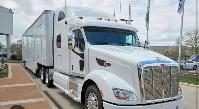 A white semi truck with a trailer attached to it is parked in a parking lot.