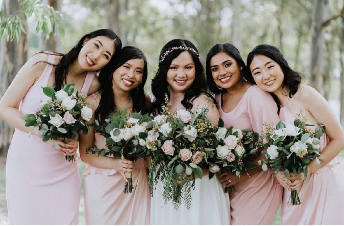 Bride and bridesmaids in pink dresses with bouquets, smiling in a park.