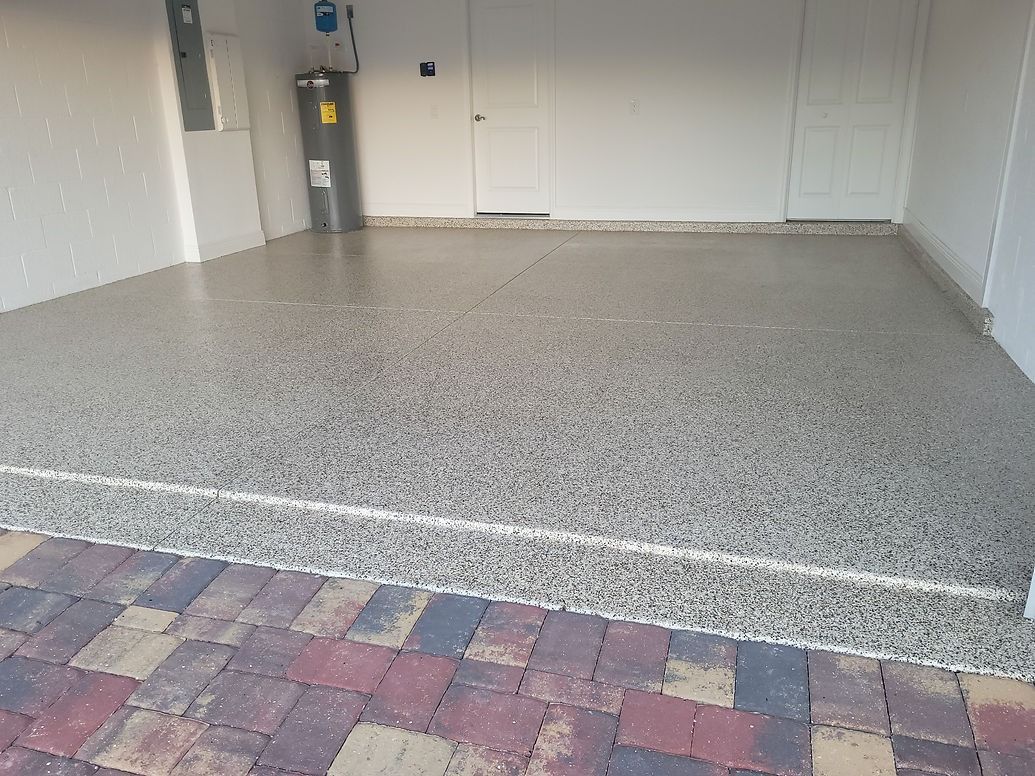 Garage with speckled epoxy floor, white walls, and brick driveway.