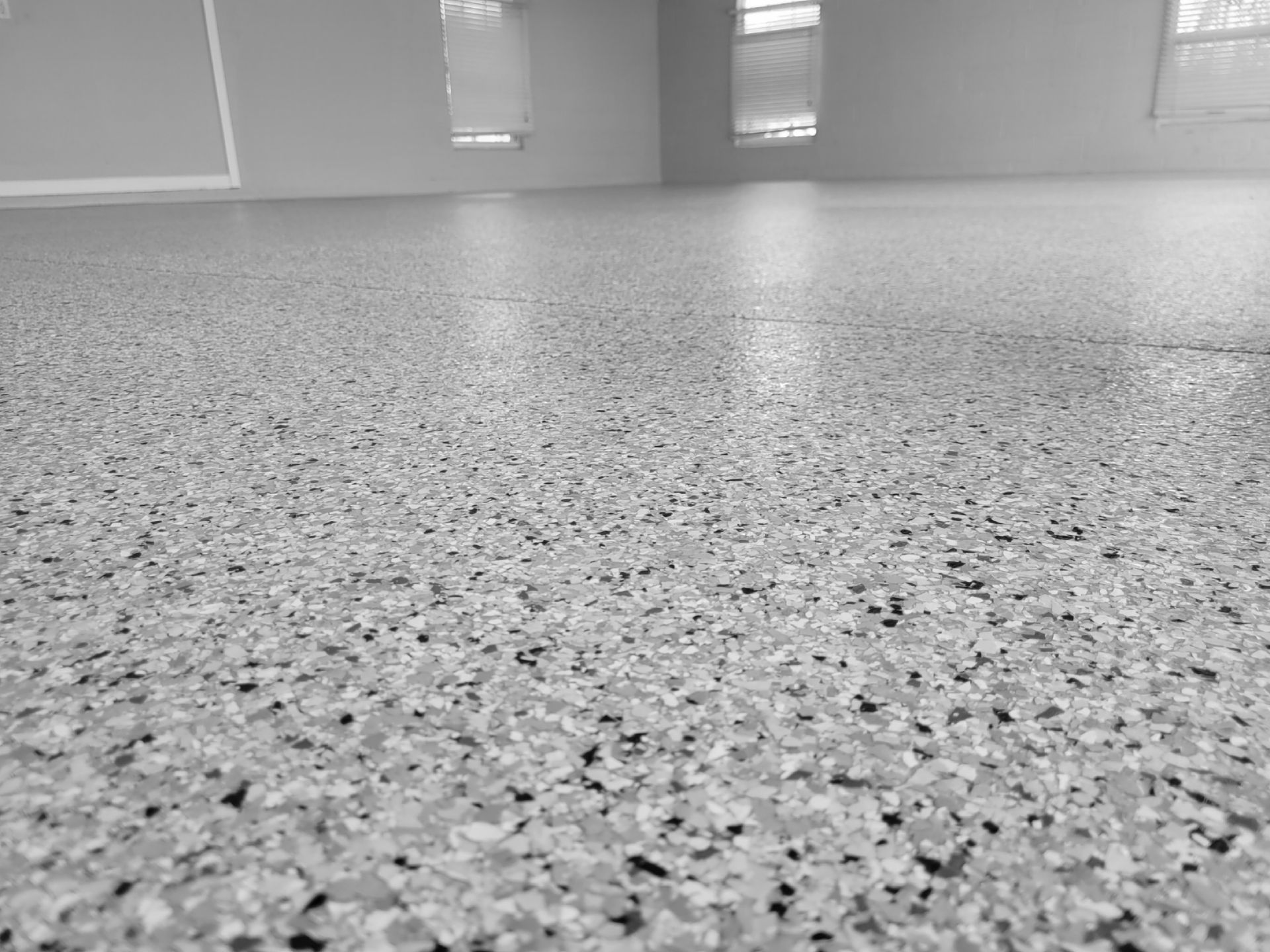 Close-up of a speckled, gray epoxy floor in a room with windows.