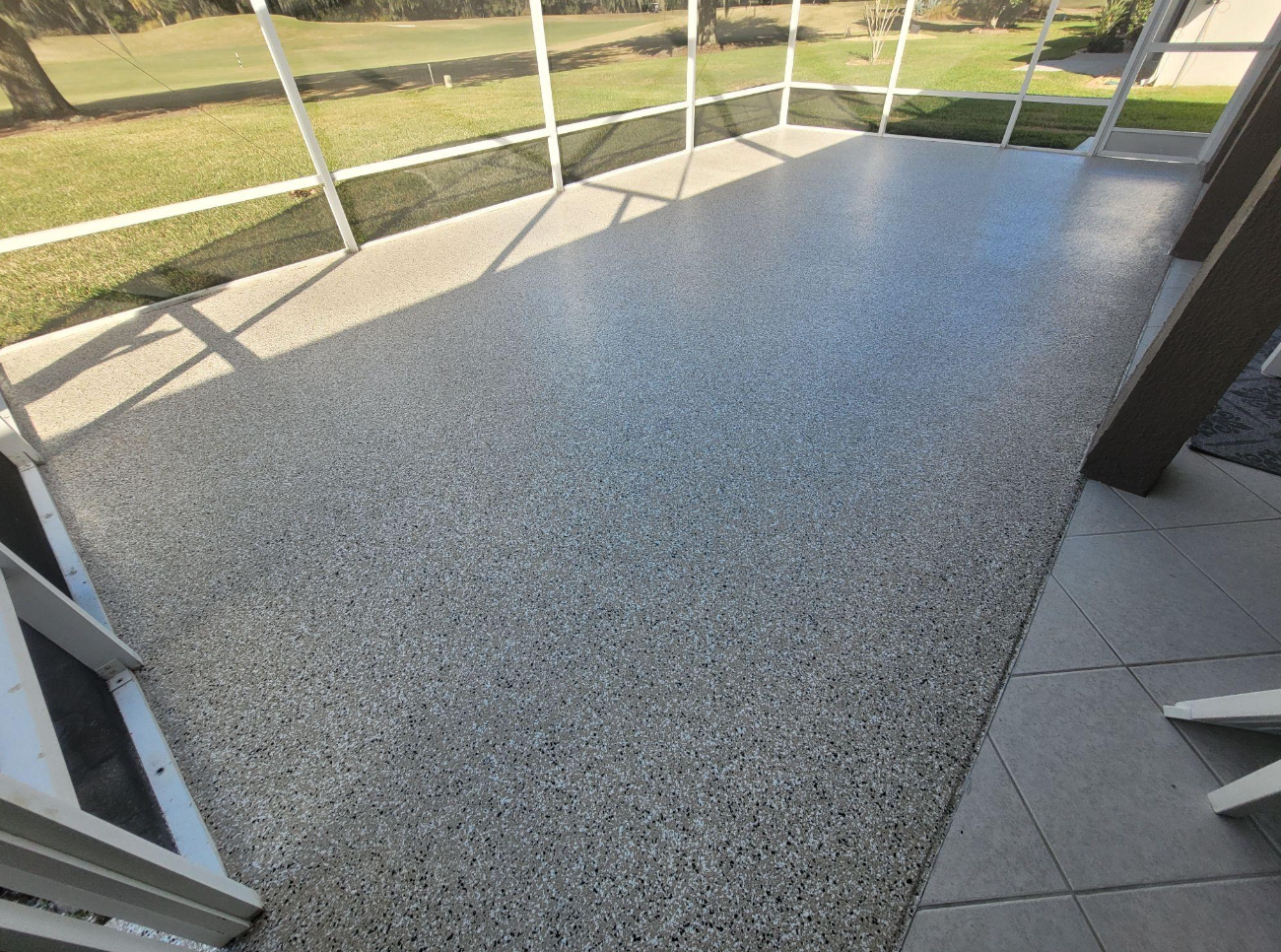 Gray speckled epoxy floor in a room, with sunlight from windows reflecting on the surface.