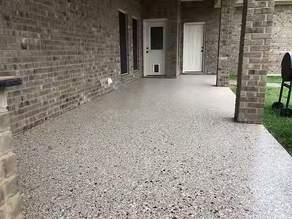 Exposed aggregate concrete patio with brick walls, doors, and a grassy area.