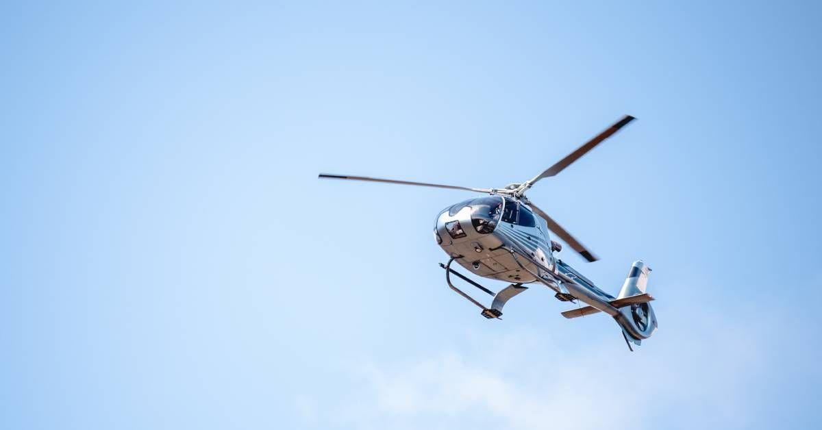 A sleek helicopter flying toward its destination alone above the ground with a massive blue sky behind it.