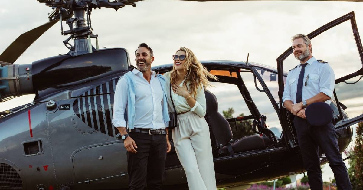 A private helicopter pilot standing by his vehicle while the couple he’s transporting exits with smiles on their faces.