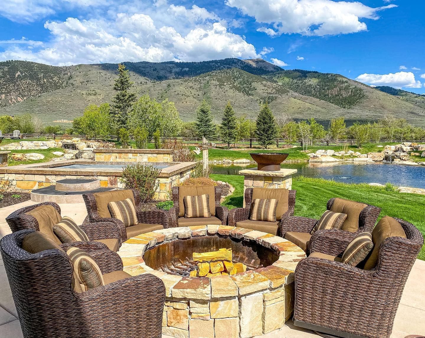 A fire pit surrounded by chairs and a couch with mountains in the background.