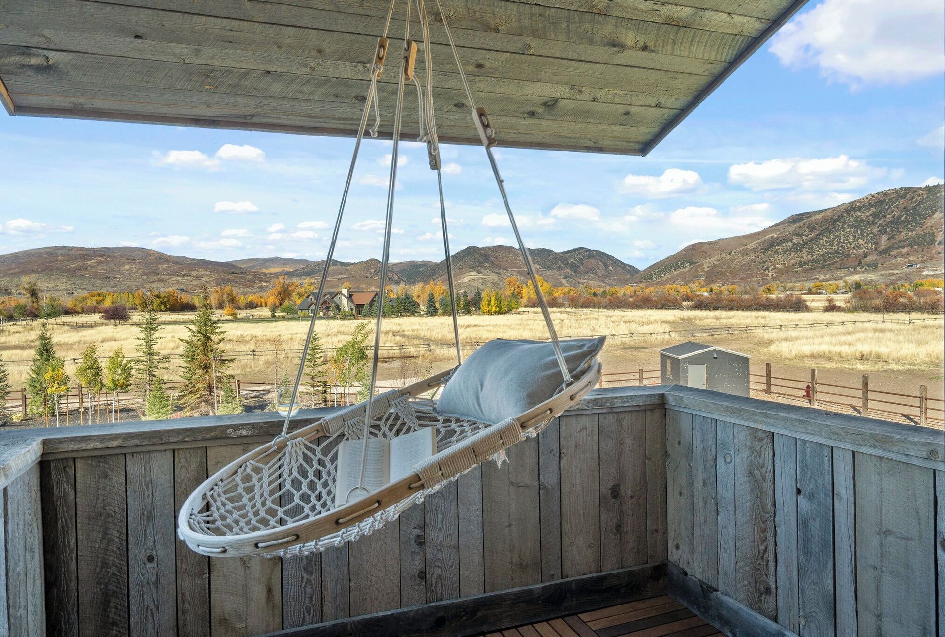 A hanging chair on a porch overlooking a scenic landscape with mountains and trees.