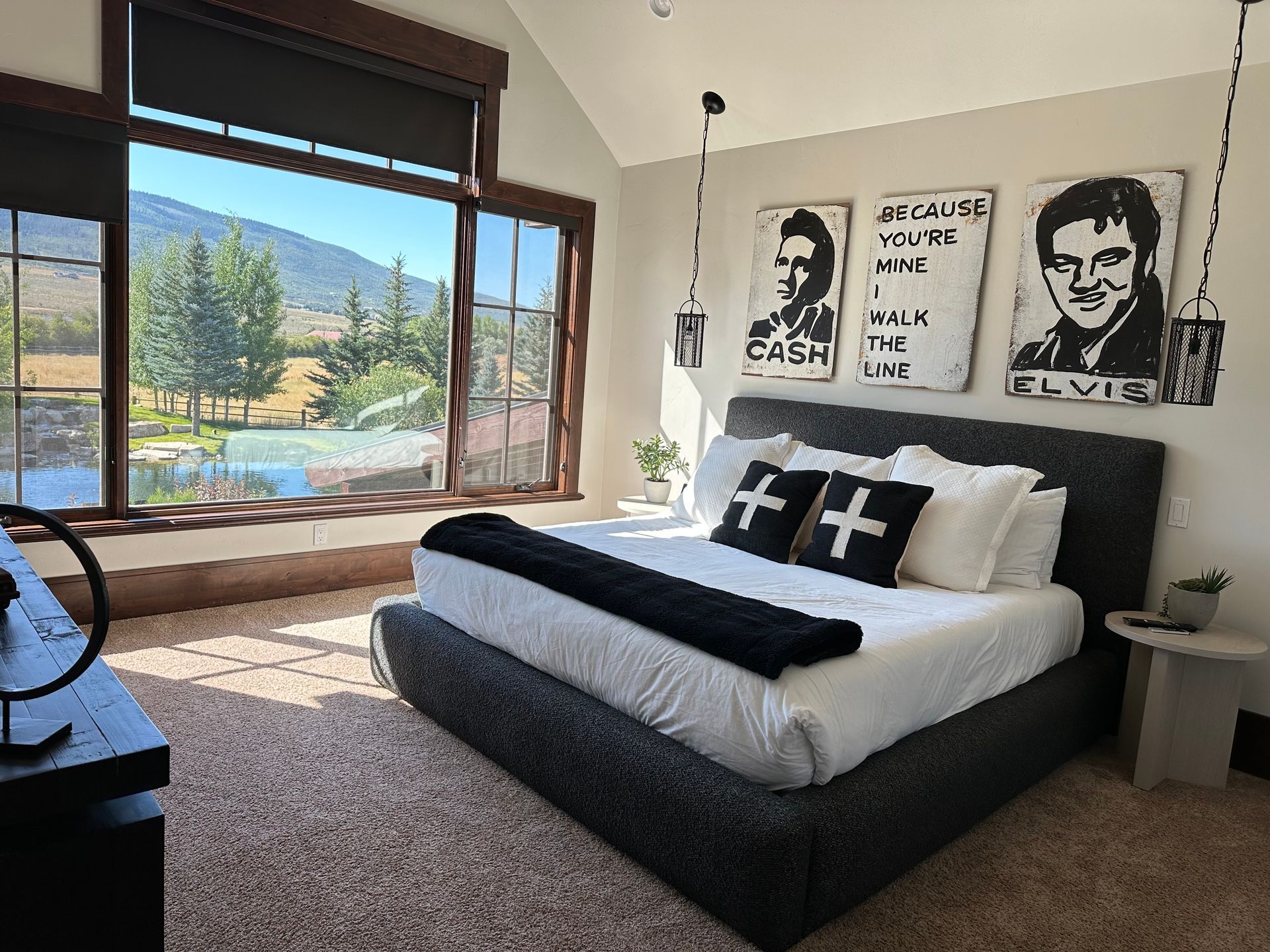Bedroom with large window overlooking a field. Elvis art above the bed, black and white decor.
