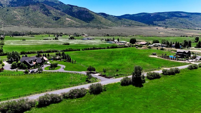Green fields with houses, road, and mountains under a bright blue sky.