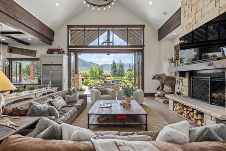 Spacious living room with open doors to the outdoors. Leather sofa, stone fireplace, and mountain view.