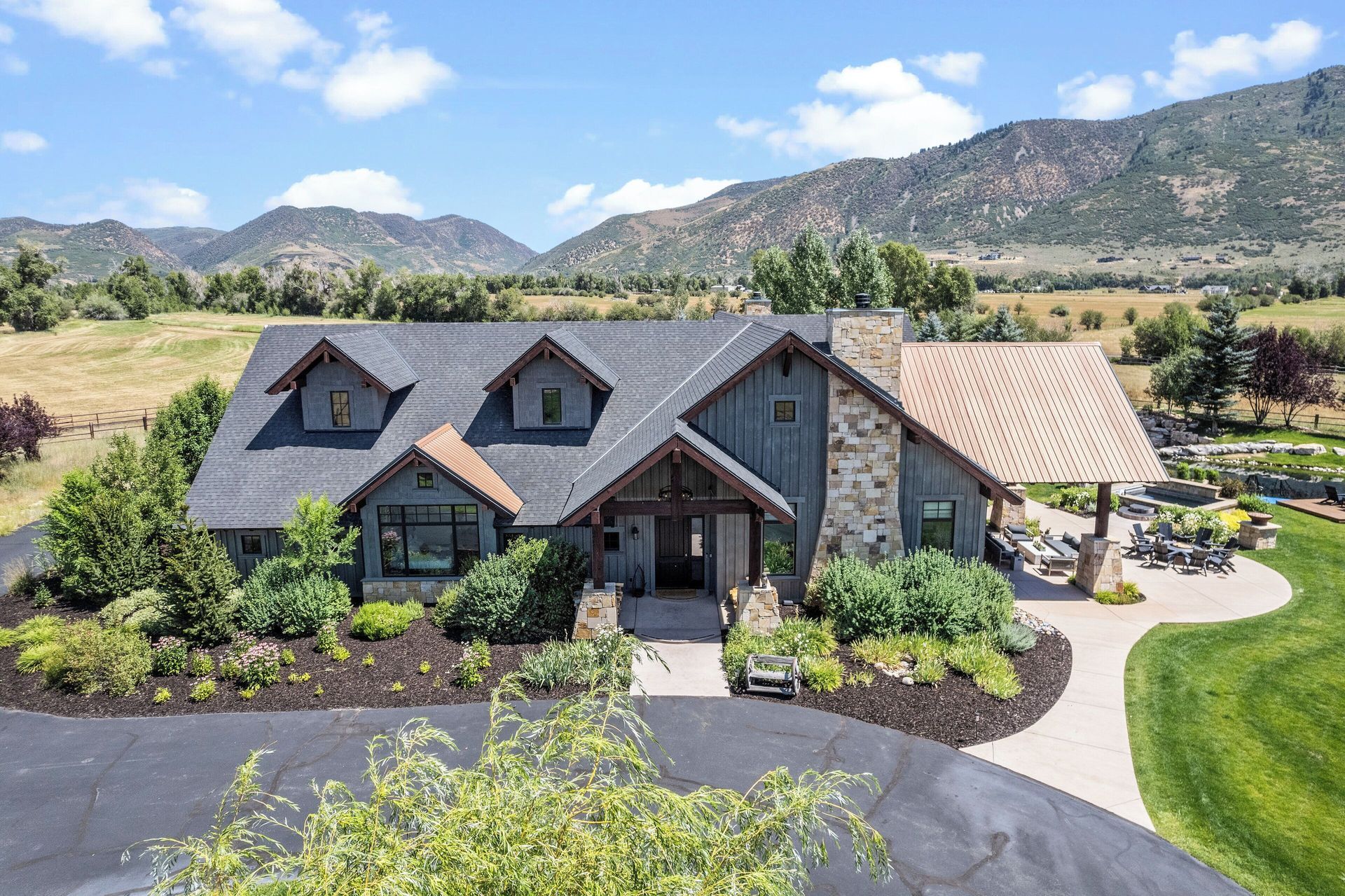 Rustic house with stone and wood exterior, surrounded by landscaping and mountains.