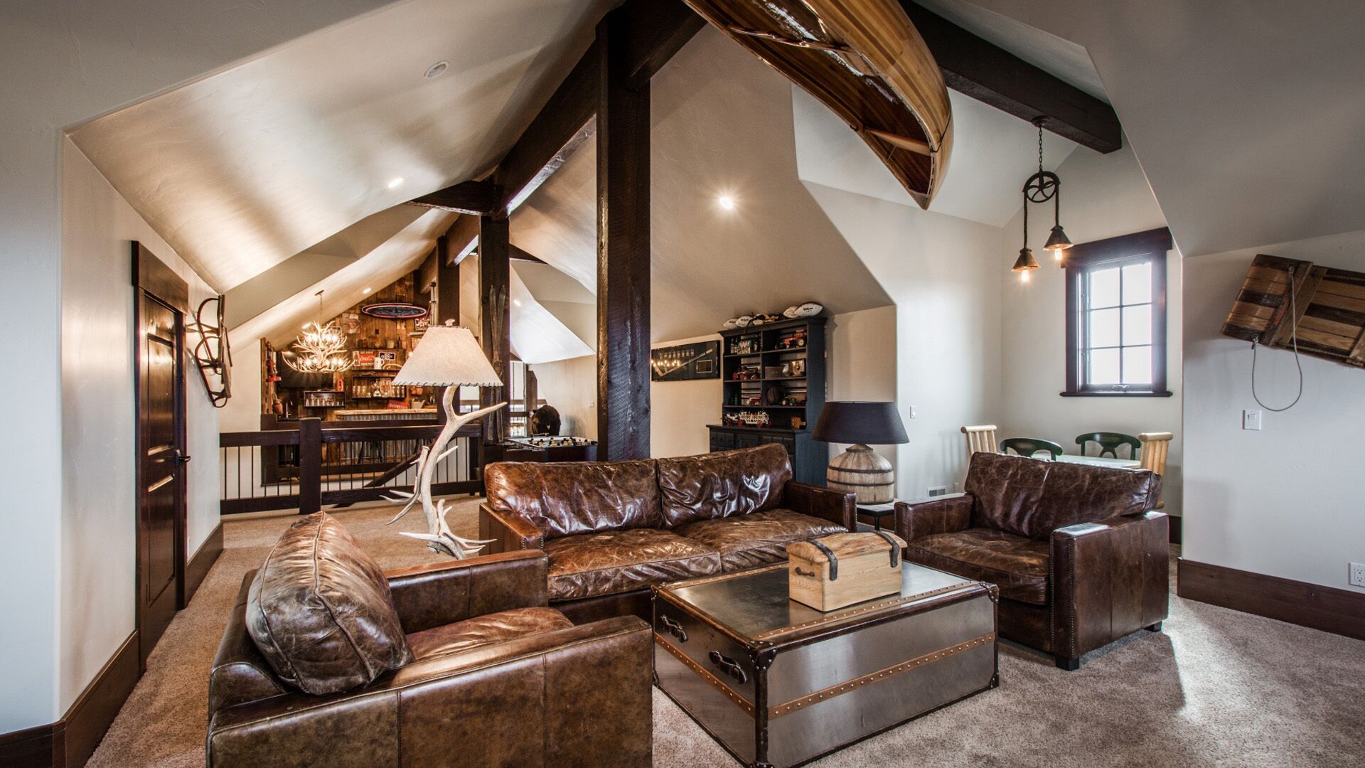 Loft with brown leather seating, canoe on ceiling, wooden beams, and a window.