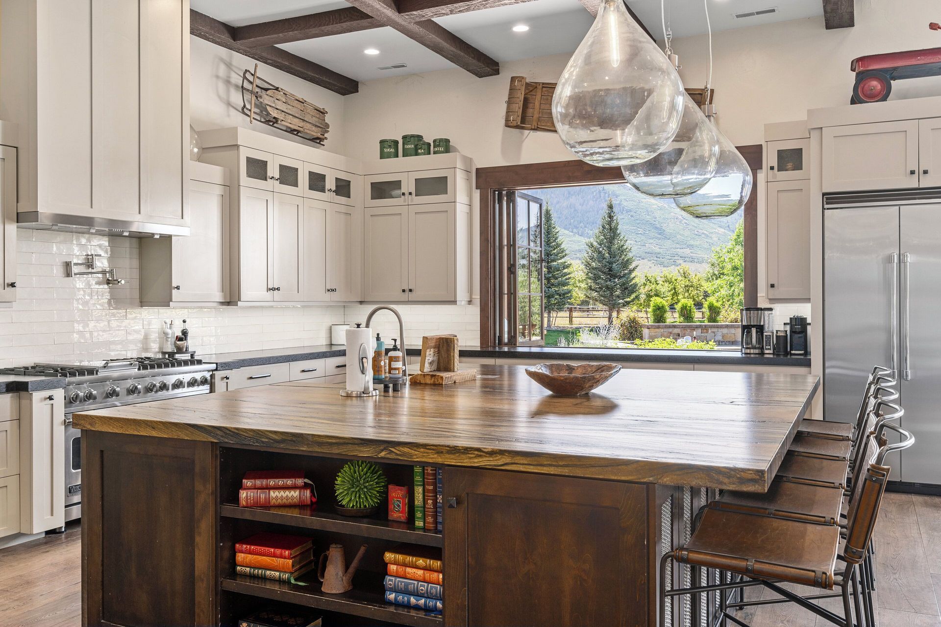 Kitchen with large island, wood beams, and open window overlooking a scenic view.