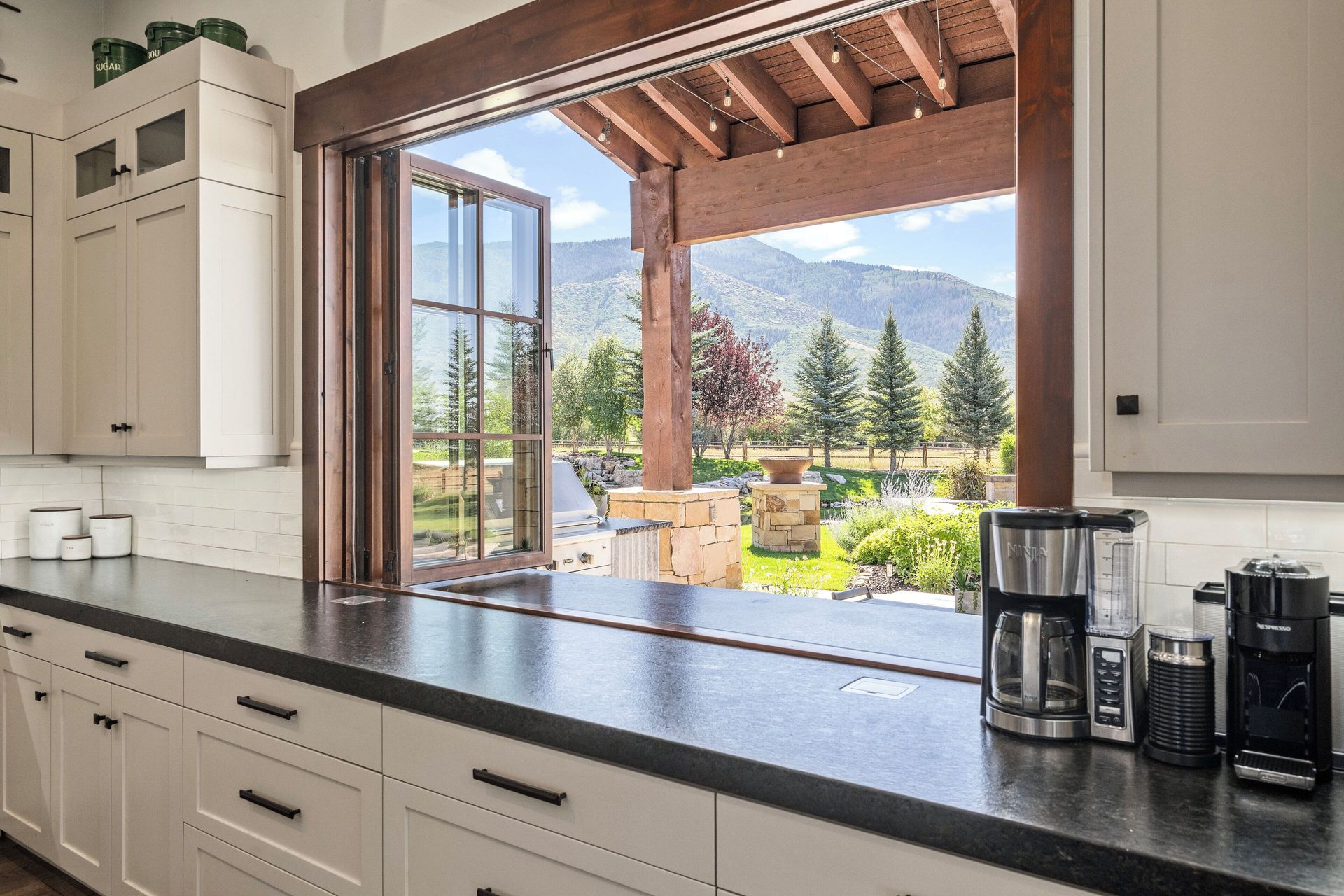 Kitchen with black countertop, opening to patio and mountain view. Coffee makers on counter.
