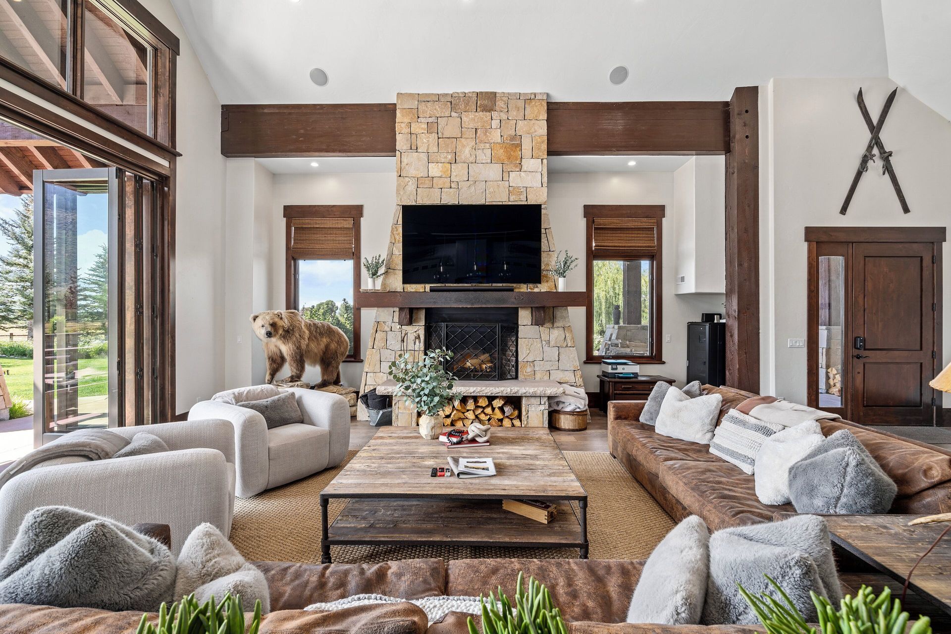 Spacious living room with fireplace, sofas, and a large bear statue. Windows and a rustic decor are present.
