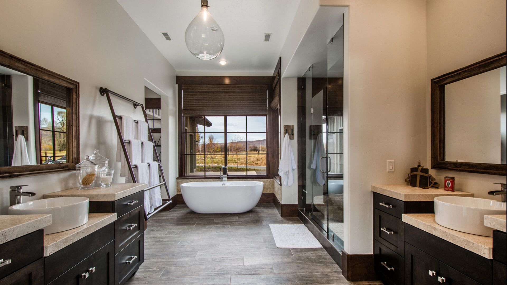 Luxury bathroom with dual vanities, large shower, freestanding tub, and scenic window view.