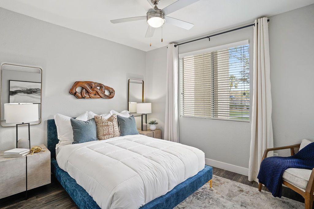 Modern apartment bedroom with a blue upholstered bed, white bedding, two nightstands, and a window with blinds.