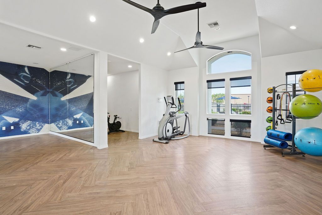 Interior community gym with treadmill, stationary bike, weight rack, mirrors, and large windows.
