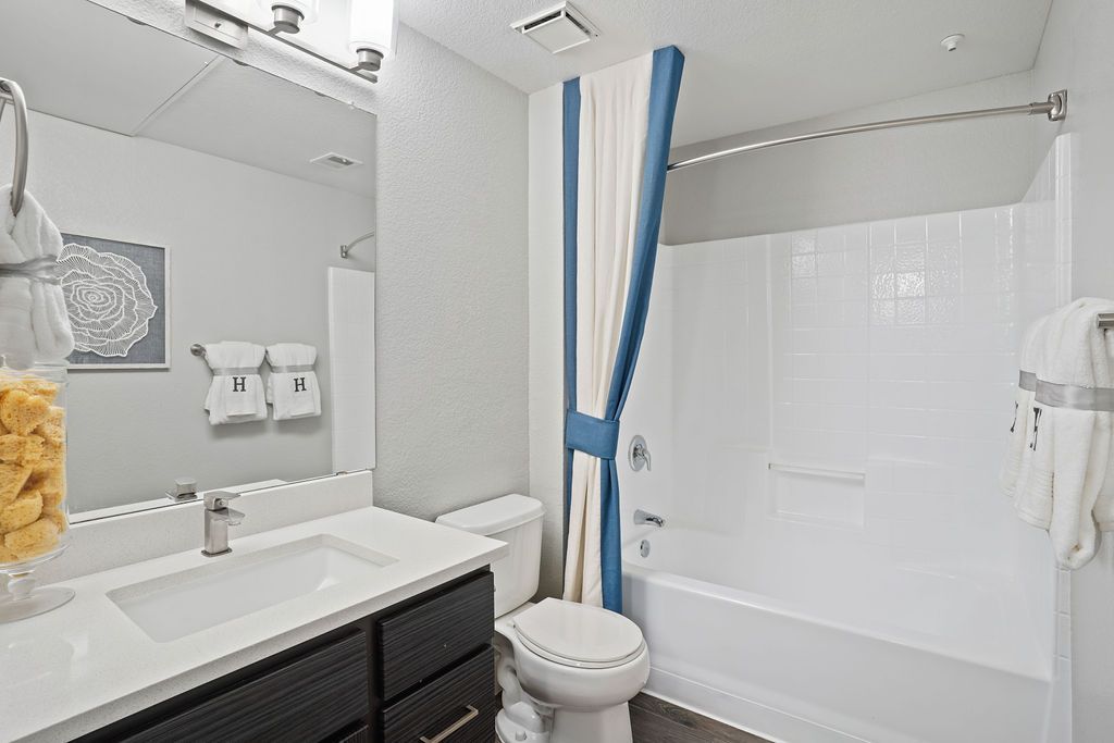 Bathroom with white sink, mirror, toilet, and tub/shower with a blue-and-white curtain.