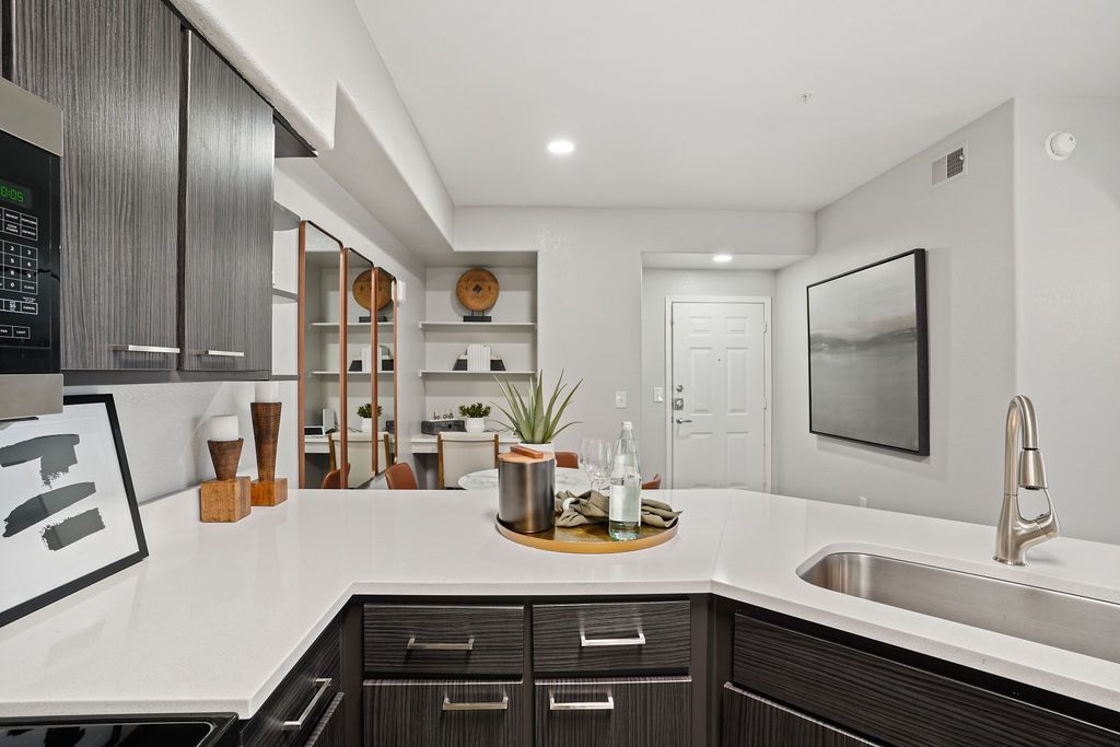 Open kitchen with white countertops, dark wood cabinets, and a stainless steel sink.