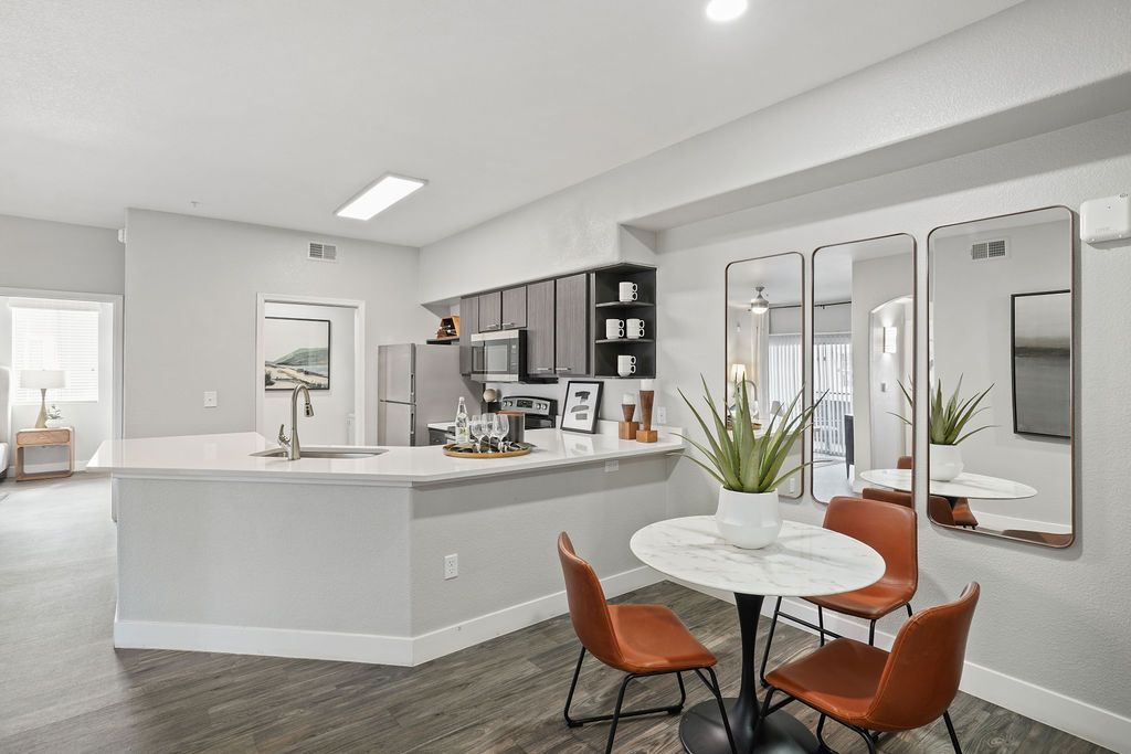 Modern apartment kitchen with white island, stainless appliances, round marble dining table, and orange chairs.