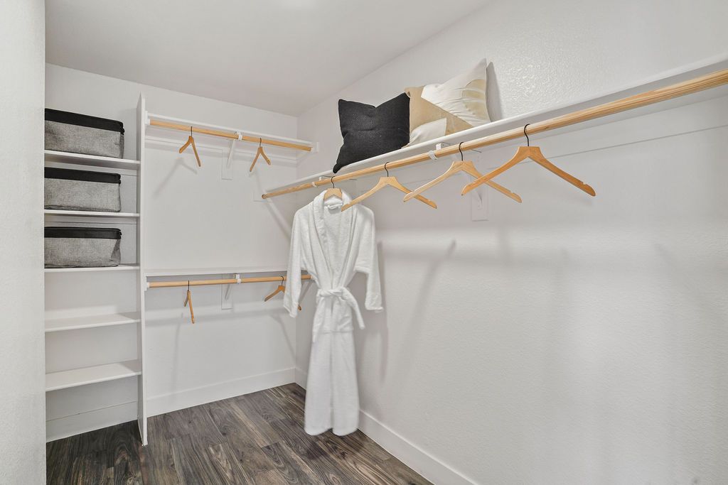 Walk-in closet with white walls, wooden shelves, and two long hanging rods.