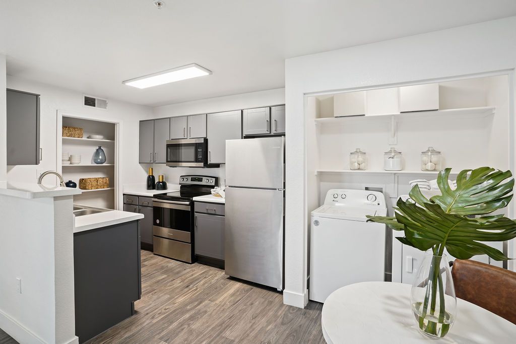 Modern apartment kitchen with gray cabinets, stainless steel fridge, stove, microwave, and a laundry alcove.