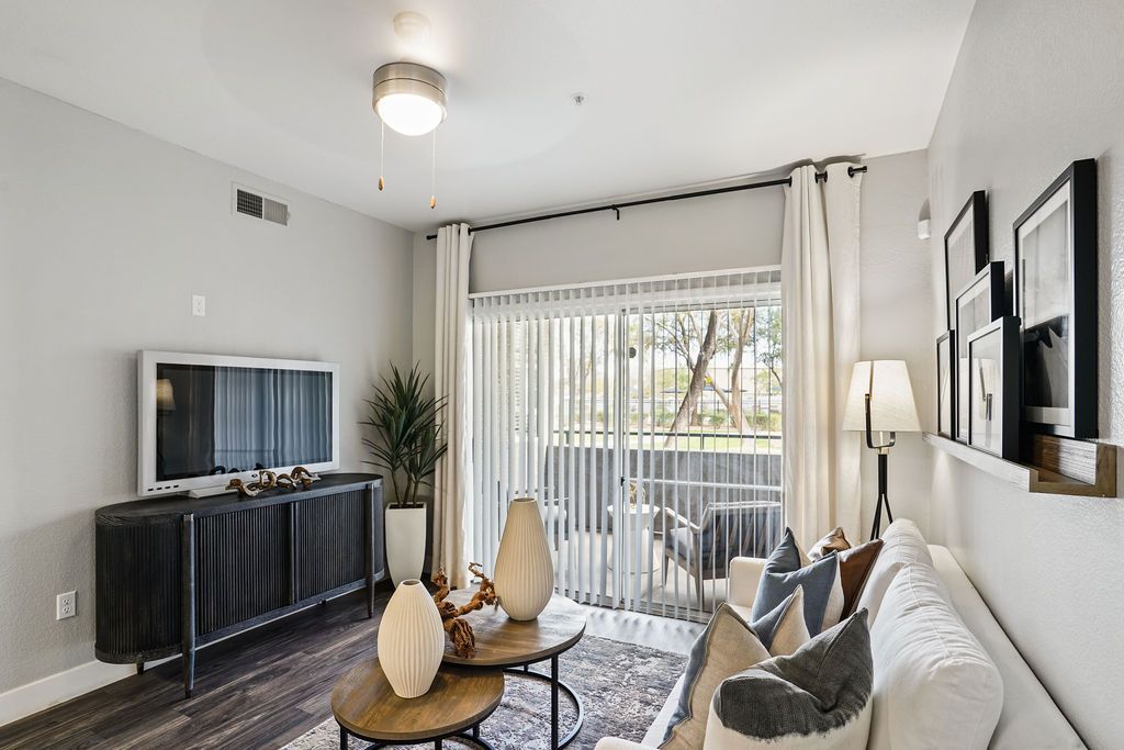 Living room in a modern apartment with a sofa, TV, and sliding glass door to a balcony.