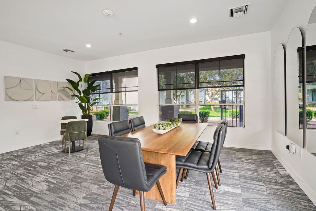 Bright communal meeting room with a wooden table, black chairs, and large windows.