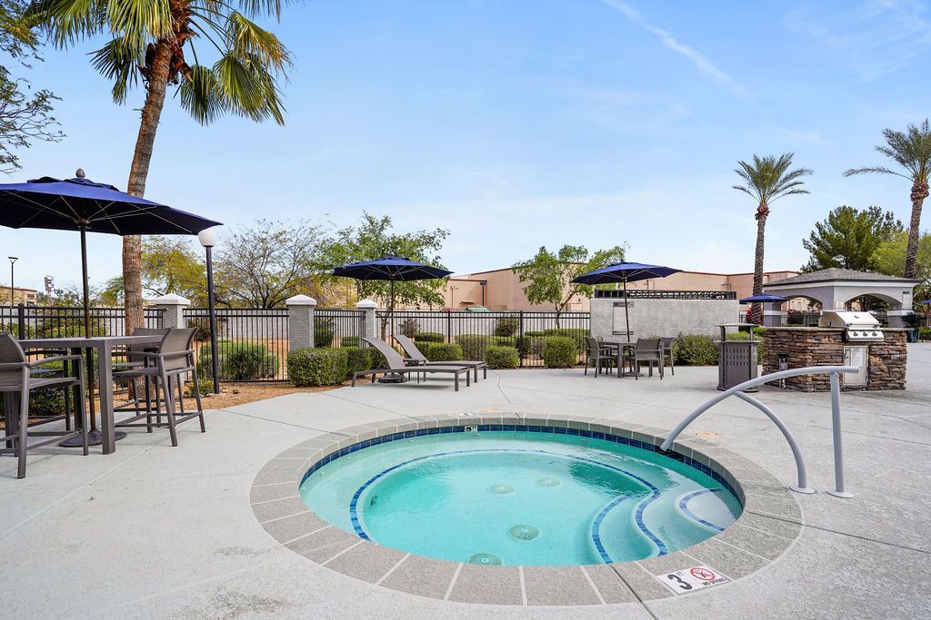 Outdoor community pool area with lounge chairs, tables, and umbrellas.