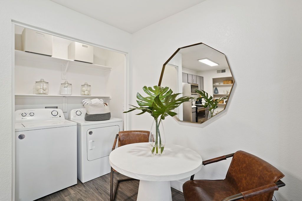 Laundry closet in an apartment with a washer and dryer, shelves, and a small round table with two chairs.