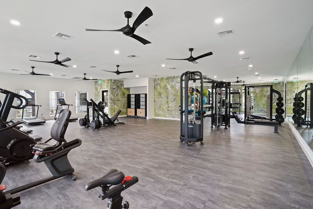 Interior of a modern fitness center with cardio machines, free weights, mirrors, and ceiling fans.