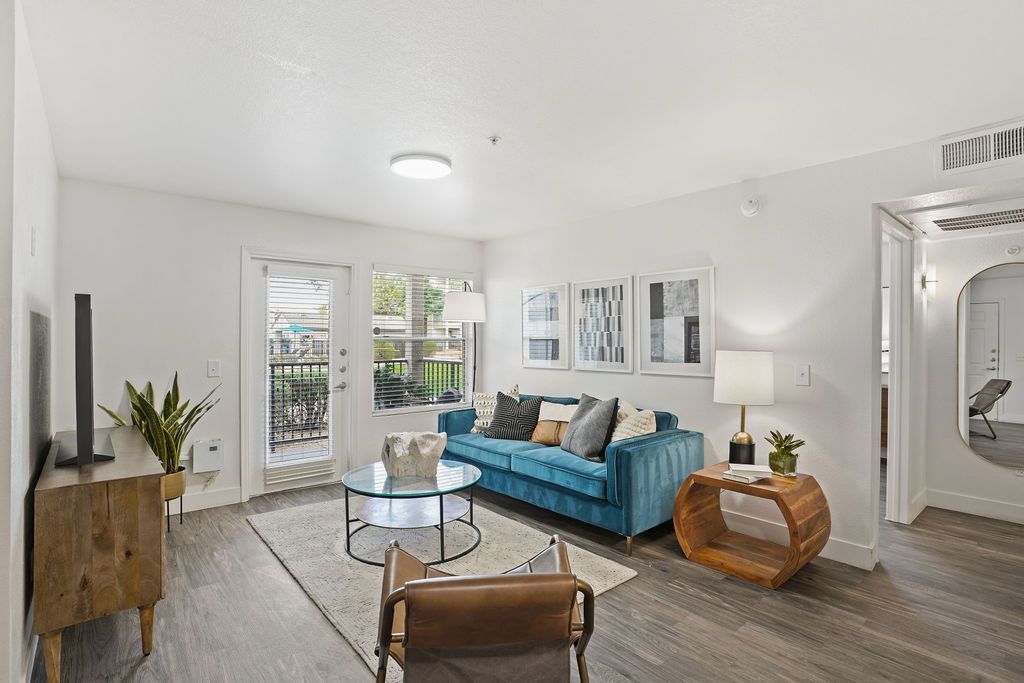 Living room with teal sofa, round glass coffee table, TV, and balcony door in a modern apartment.