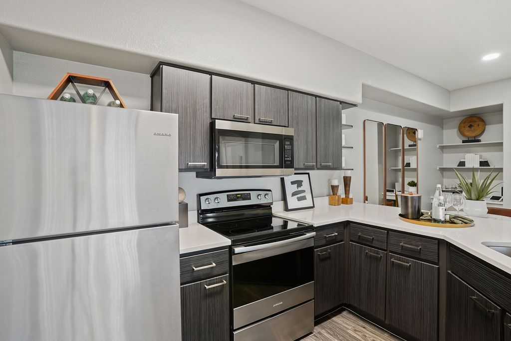 Modern apartment kitchen with stainless steel refrigerator, microwave, stove, and dark wood cabinets.
