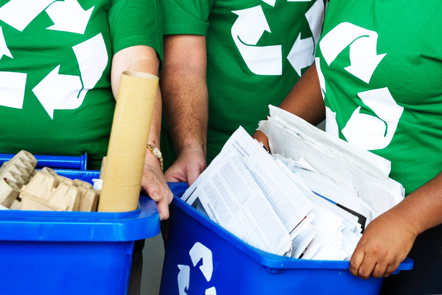 People in green shirts sort paper and cardboard into blue recycling bins.