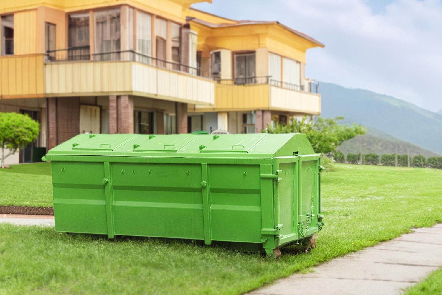 A green dumpster is parked in front of a house.