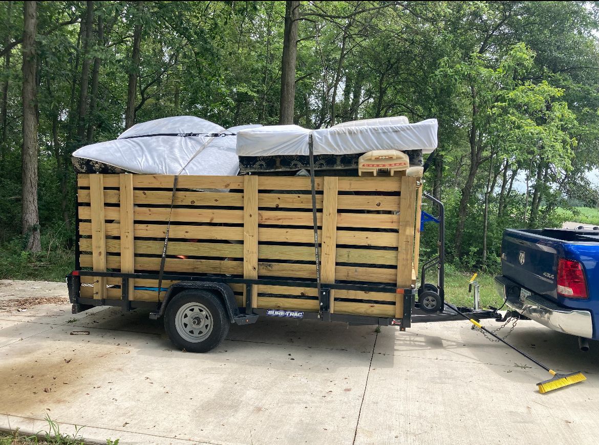 A wooden trailer filled with furniture is hitched to a blue pickup truck on a driveway.